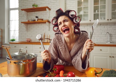 Desperate housewife sick and tired of cooking and housework crying in the kitchen. Unhappy overworked young woman in hair rollers and bathrobe complaining about everyday cooking food and cleaning home