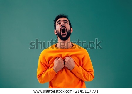 desperate man screaming out loud putting his fist hands to his chest - caucasian person with orange sweater on green background