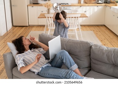 Desperate Mom Ask Son To Be Silent Surf Internet On Laptop For Work. Young Single Mother Freelancer Or Remote Worker Work From Home With Naughty Little Kid. Parent And Child On Covid Pandemic Lockdown