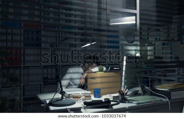 Desperate office worker packing\
his belongings after being fired, he is holding a cardboard\
box