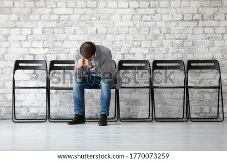 Desperate sad jobless man put head on hands sitting on chair hunched after unsuccessful failed job interview meeting. Fired employee feels stressed after dismissal, boss and company bankruptcy concept
