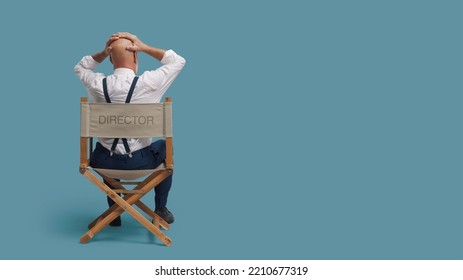 Desperate Stressed Film Director With Head In Hands, He Is Sitting On The Director's Chair, Back View