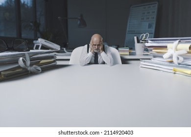 Desperate tiny office worker sitting at desk with head in hands, overtime work and business failure concept