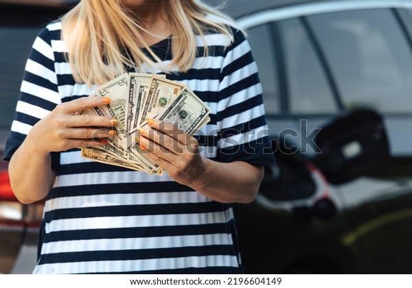 Desperate woman hold cash dollar\
bills next to car with an open tank, concept of rising fuel\
prices