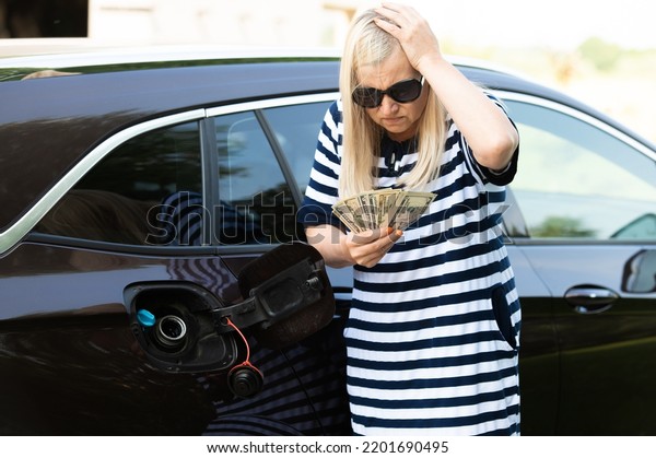 Desperate woman hold cash dollar\
bills next to car with an open tank, concept of rising fuel\
prices