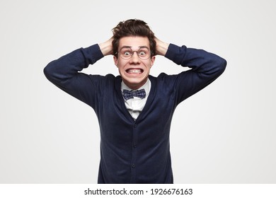 Desperate young businessman in stylish outfit and glasses getting shocked with news about financial crisis and making grimace on white background