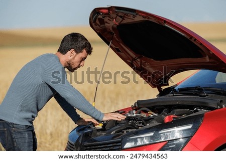 Desperate young man with broken down car in the middle of the road, dead battery