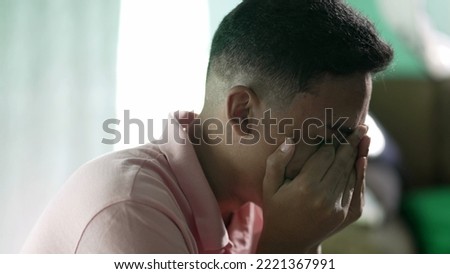 Desperate young man feeling hopeless and despair. A hispanic South American person crying covering face with hand