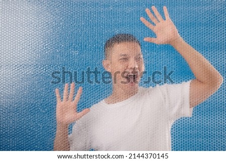 Desperate young man shouting behing bubble wrap wall