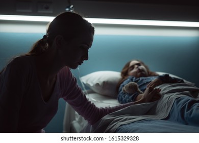 Desperate Young Mother Assisting Her Sick Child Lying In A Hospital Bed At Night