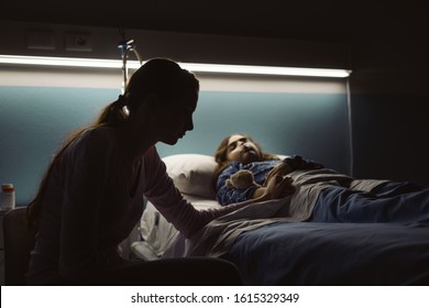 Desperate young mother assisting her sick child lying in a hospital bed at night - Powered by Shutterstock