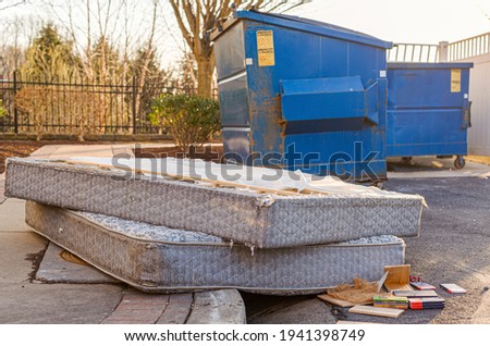Despite HOA regulations by the Home owners association, residents still illegally dump bulk items by the residential trash containers. Two old mattresses left behind by dumpster create unsightly look.