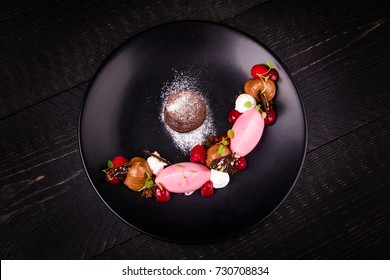 Dessert With Chocolate Cake, Mousse And Raspberry On A Black Plate On A Dark Wooden Background, Top View

