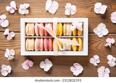 Dessert French Macarons in present box. Sweet dessert on a flowers background. Still life with macaroni cakes and different flower. Delivery concept, coffee and flower shop