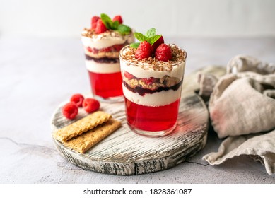 Dessert in a glass cup, with Jello covered in yogurt and topped with fresh raspberries. Mini dessert on light concrete background. Fruit parfait with jello and jelly.