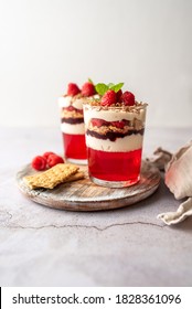 Dessert in a glass cup, with Jello covered in yogurt and topped with fresh raspberries. Mini dessert on light concrete background. Fruit parfait with jello and jelly.