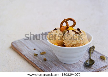 Dessert, homemade ice cream or frozen yogurt with persimmons, decorated with salted pretzels and grated chocolate, in a white bowl on a light concrete background. Selective focus.