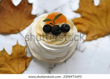 Dessert pavlova with fruits on the white plate, yellow autumn leaves on the marble background. Horizontal arrangement
