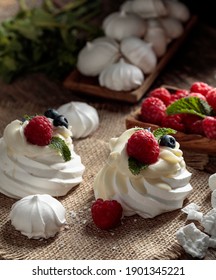 Dessert Pavlova with raspberries, blueberries and mint. Dessert Pavlova and small meringues on a rustic background.