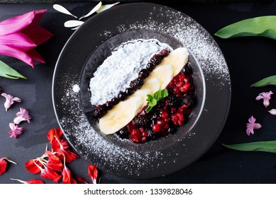 Dessert Salade Of Yogurt, Bannana, Wild Berries, And Leaves Of Mint, On Black Plate  Surrounded By Flowers