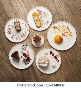 Dessert table with cupcake, mousse, biscuits, cheesecake. Piece of cakes on a white plate on wooden table background 