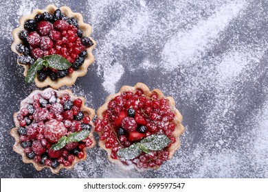 Dessert Tartlets With Berries And Powdered Sugar On Grey Wooden Table