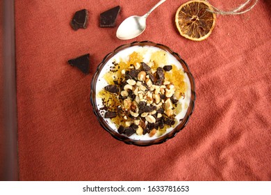 Dessert Yogurt Bowl With Orange Marmalade, Dark Chocolate And Hazelnuts On Red Background, Top Down View