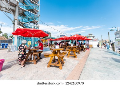 Destin, USA - April 24, 2018: City town Harborwalk village Harbor Boardwalk during sunny day in Florida panhandle gulf of mexico, tourists people sitting on chairs in restaurant outdoor tables