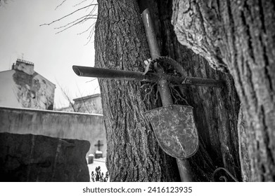 A destroyed iron cross, leaning against a large hole in a tree in the cemetery, black and white