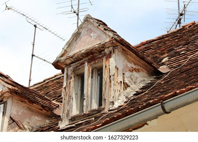 Destroyed Old Roof Windows With Cracked Wooden Frame On Top Of Old Ruins Of Abandoned Suburban Family House Surrounded With Broken Roof Tiles And Multiple TV Antennas