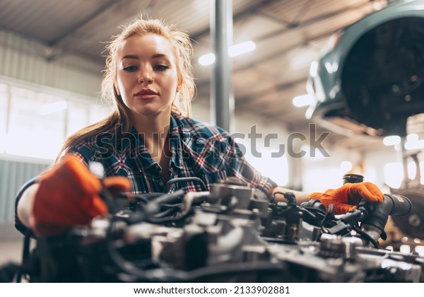 Destroying\
gender stereotypes. Young woman auto mechanic working at auto\
service station using different work tools. Gender equality. Work,\
occupation, car. Pretty girl in work\
clothes