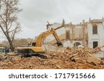 The destruction of an old building. Yellow excavator breaks down walls. Heaps of construction debris and dust. 