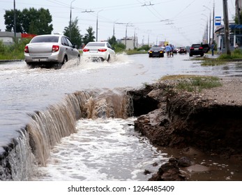 Destruction of the road after heavy rain. Water falls into a huge deep hole. Cars driving on a deep puddle