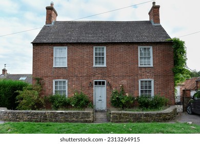 Detached double fronted 
						red brick Victorian cottage with a green door in an English village
