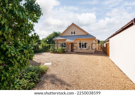 Detached house with large gravel driveway bathed in sunshine viewed from public highway