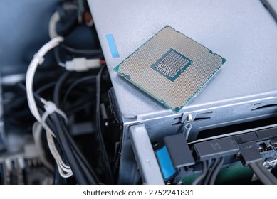 Detached processor resting on open server equipment. Microchip placed above metal chassis and internal wiring. Computer upgrade concept with loose central processing unit. Technology maintenance scene showing hardware replacement part