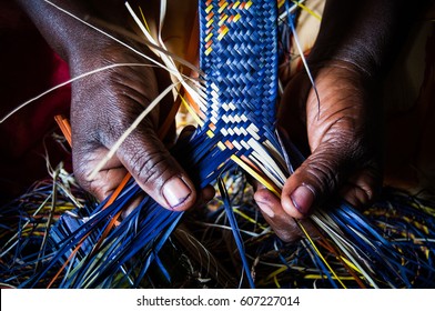  Detail of African woman's hands weaving blue and yellow raffia mat - Shutterstock ID 607227014