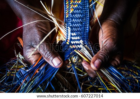  Detail of African woman's hands weaving blue and yellow raffia mat