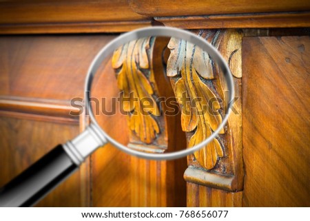 Detail of an antique wooden italian furniture just restored with a magnifying glass on foreground looking for woodworm threat detection