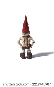 Detail Back Shot Of A Designer Figurine Of A Skeleton Of A Dwarf Man In A Red Hat And A Brown Loincloth. The Original Handmade Statuette Is Isolated On The White Background.                          