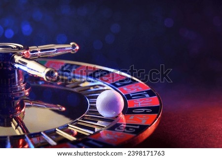 Detail of ball fixed on the black six of a casino roulette wheel on table and dark isolated background with soft red and blue lighting in the dark.