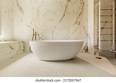 Detail Of A Bathroom With Marble Walls, A Continuous Worktop In The Same Material, Brass Taps, A White Towel-drying Radiator And A Freestanding White Bathtub