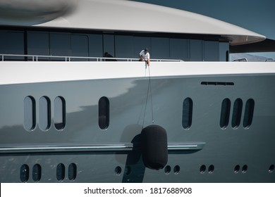 Detail of beautiful Superyacht, deckhand lifting the huge fender of the starboard side of the megayacht, spotless grey and white superstructure
