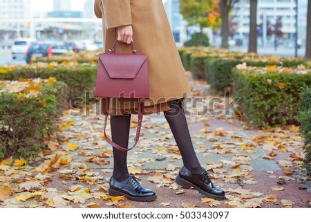 Detail of a beautiful young fashion woman wearing beige coat with flower brooch and  skirt with handbag in the city streets . Street style .