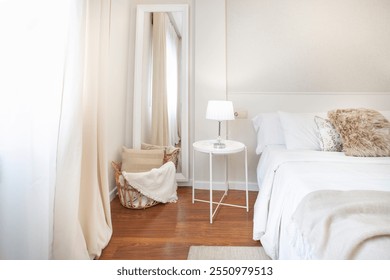 Detalle de un dormitorio con una cama, cortinas, mesa de metal, lámpara blanca, Grande espejo blanco, cesta de mimbre, cojín de piel marrón, piso de madera natural, pared blanca, habitación brillante