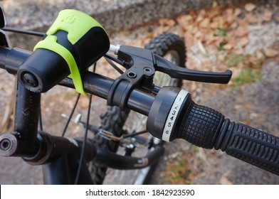 Detail of the black aluminum handle bar of a mountain bike, with a closer view on the brake lever and the gear shifter on the right side, connected to cables, and the headlight closer to the axis