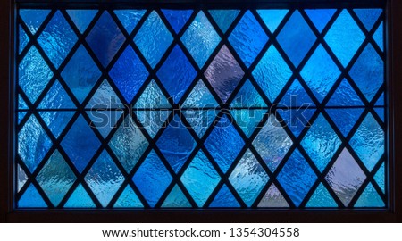 Detail of blue diamond shaped panes in colored light from stained glass window in catholic church