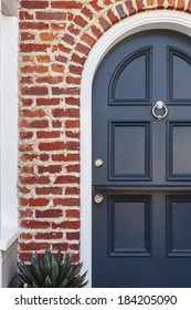 Detail Of Blue Door To Classic Brownstone Home. Detail Of A Lacquered Blue Front Door To A Classic Brownstone Family Home. Door Is Featured Under Brick Arch, With Door Knocker, And A Plant. 