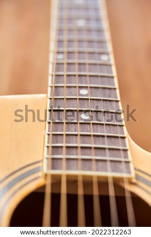 Detail of the body of a light wood electroacoustic guitar, the soundhole, the fretboard and the strings. Close-up vertical image with shallow depth of field.