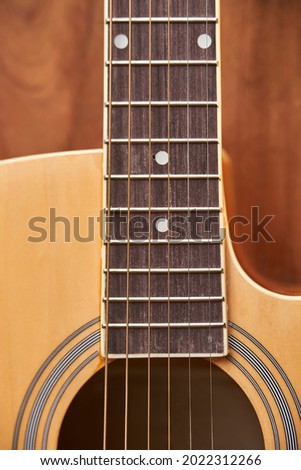 Detail of the body of a light wood electroacoustic guitar, the soundhole, the fretboard and the strings.